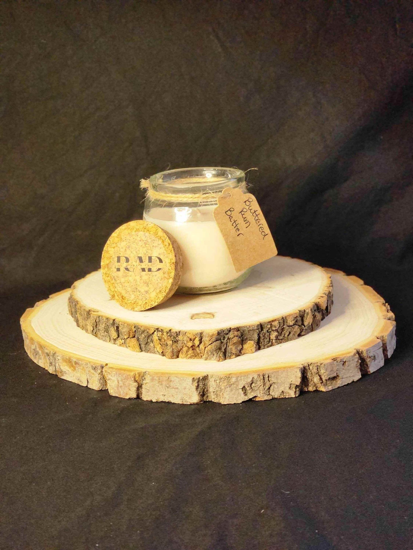 Buttered Rum scented soy candle in a glass jar on a wooden slice base, cozy and inviting decoration.
