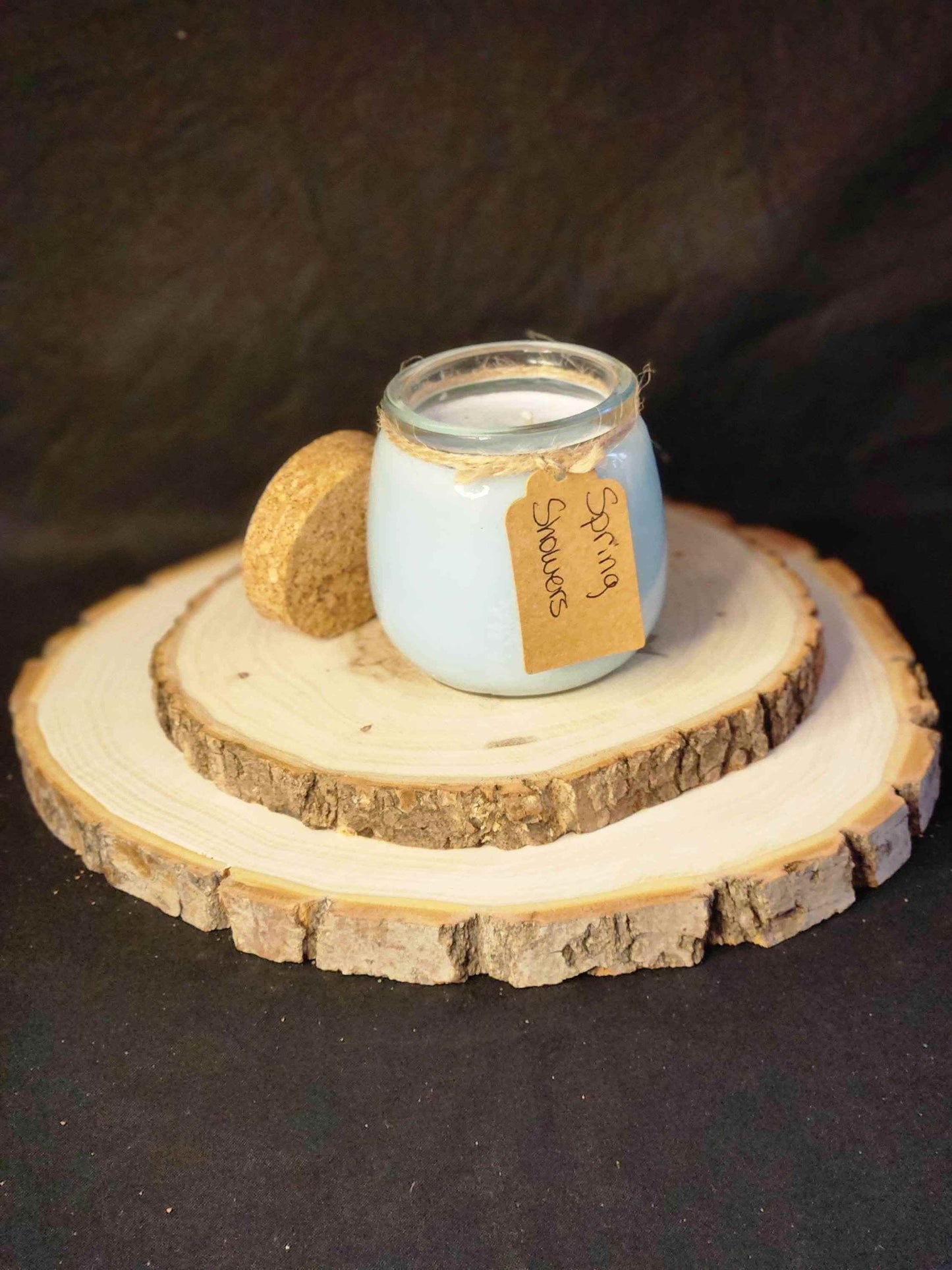 Spring Showers scented candle in a glass jar on a wooden slice, featuring a tag and a cork lid.
