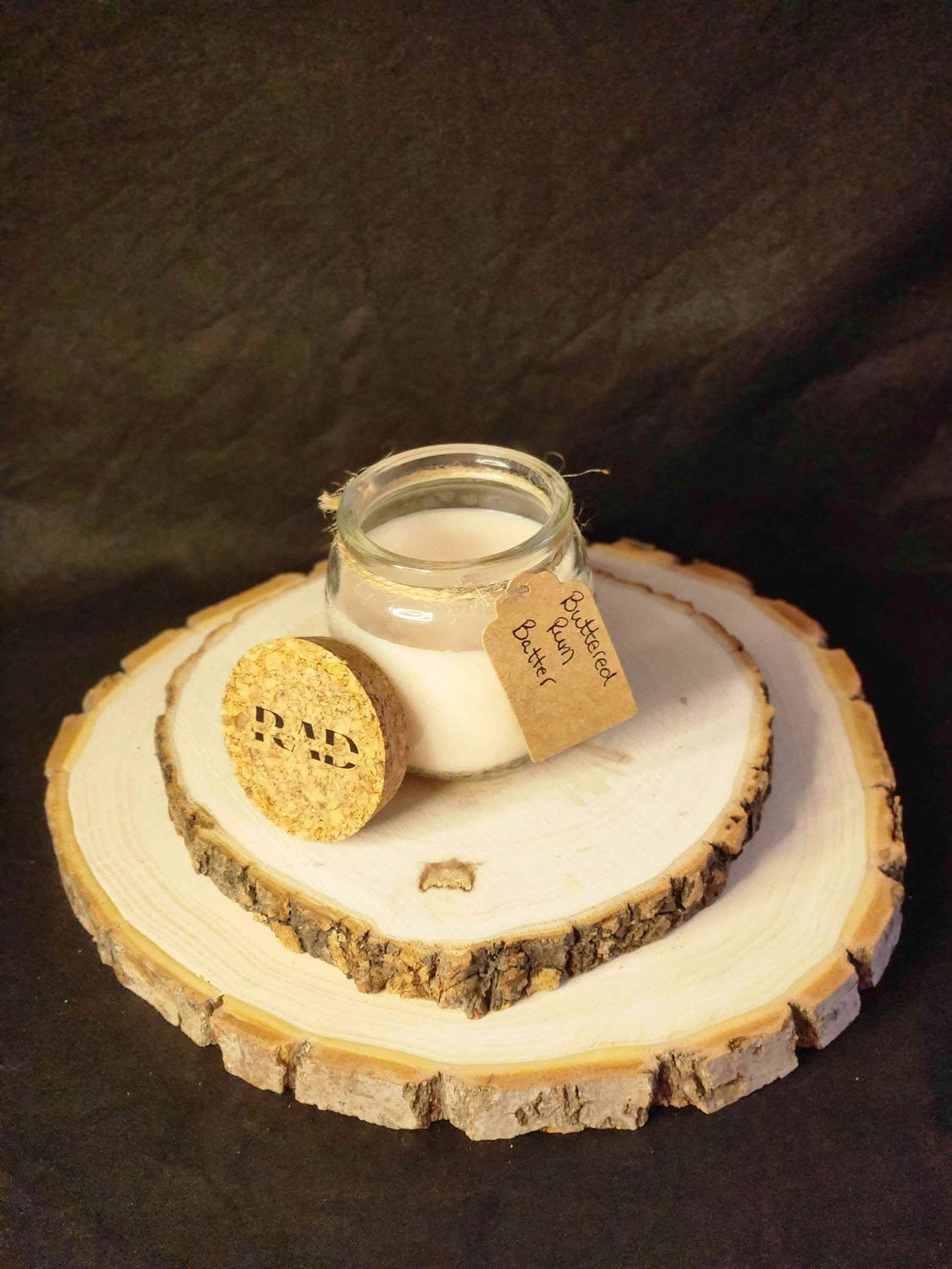 Buttered Rum Scented Soy Candle on a natural wood display, featuring a rustic cork lid and handmade label.