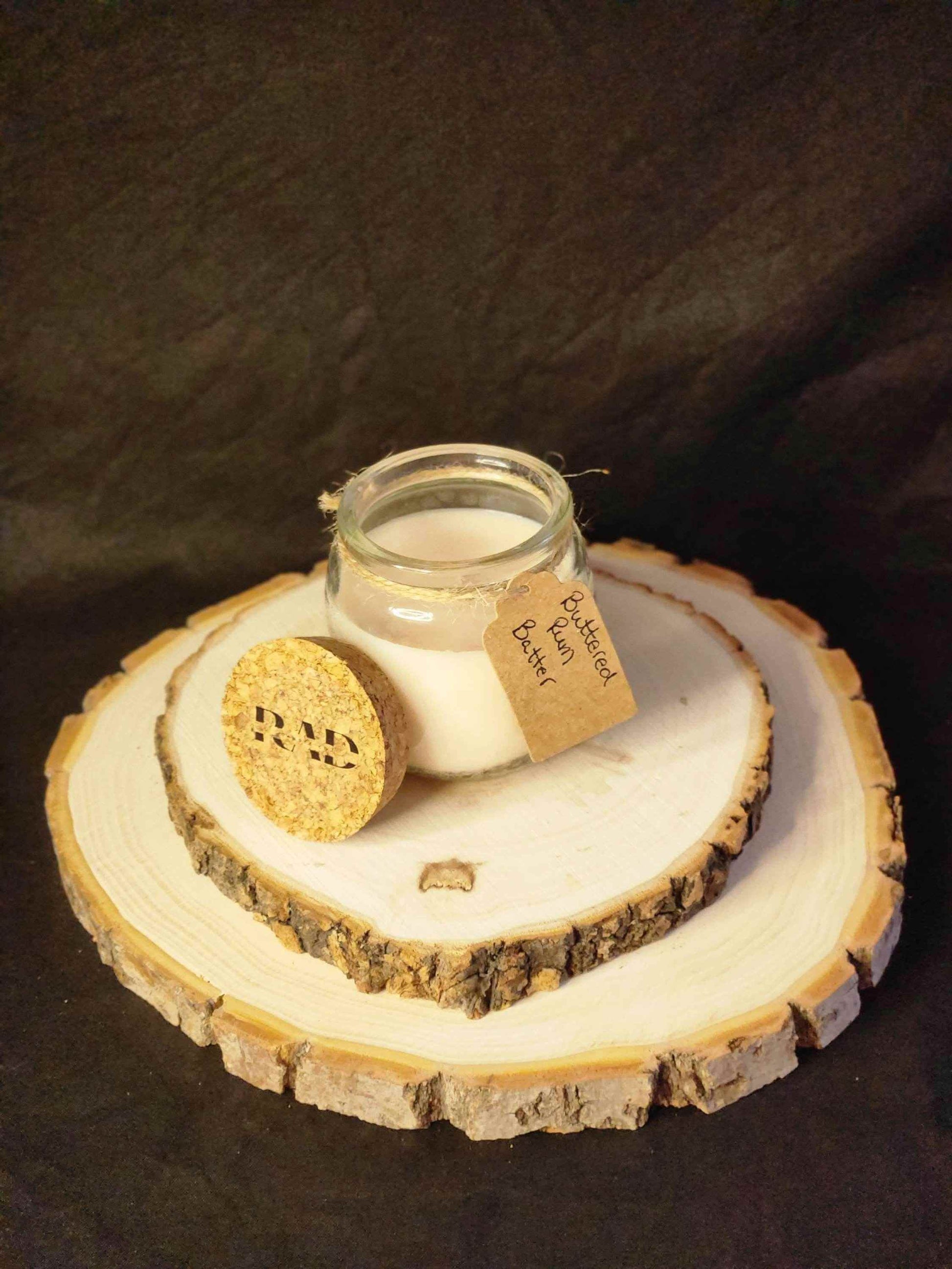 Buttered Rum Scented Soy Candle on a natural wood display, featuring a rustic cork lid and handmade label.